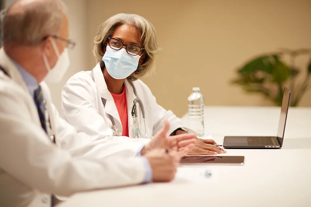 Female and male physicians in masks having a conversation at a conference table