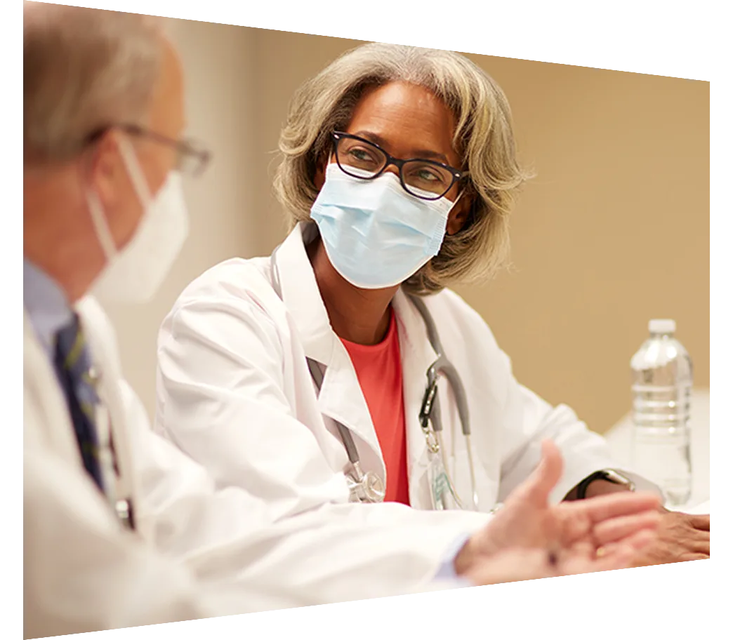 Female and male physicians in masks having a conversation at a conference table