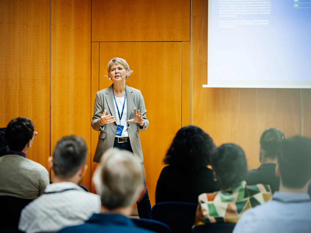 Woman standing in front of an audience presenting.