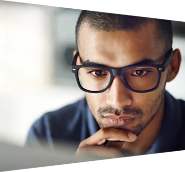 A thoughtful-looking man wearing glasses looking at a monitor