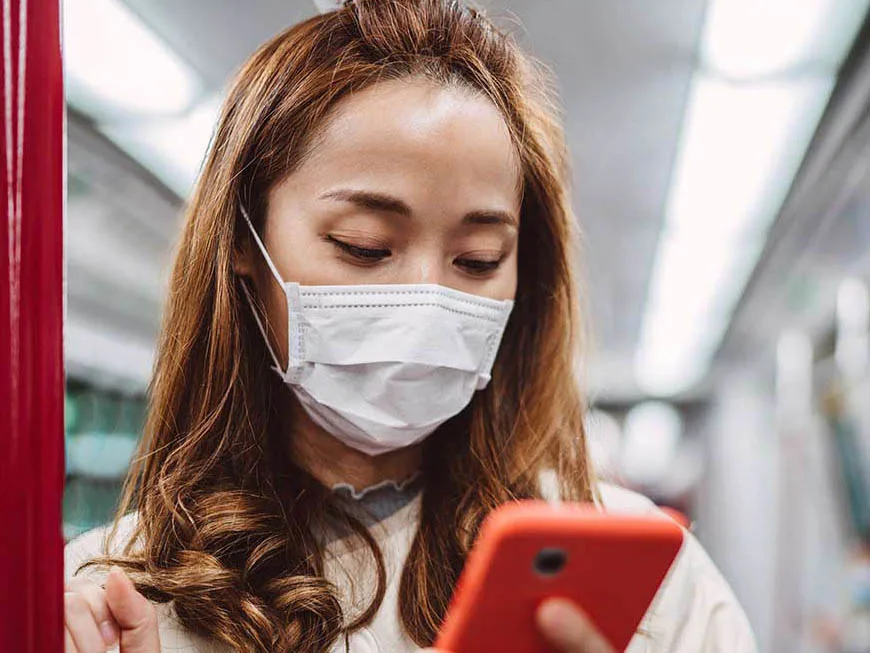 Woman wearing facemask with smartphone on train 