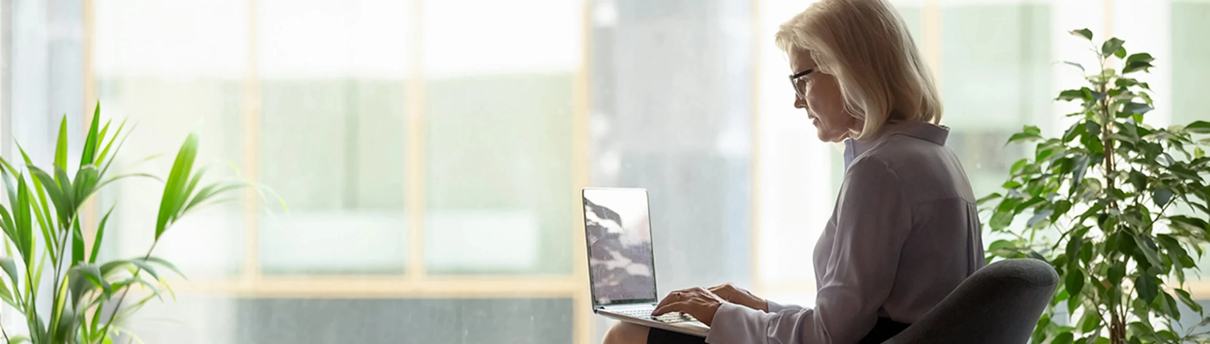 Woman sitting next to window working on laptop