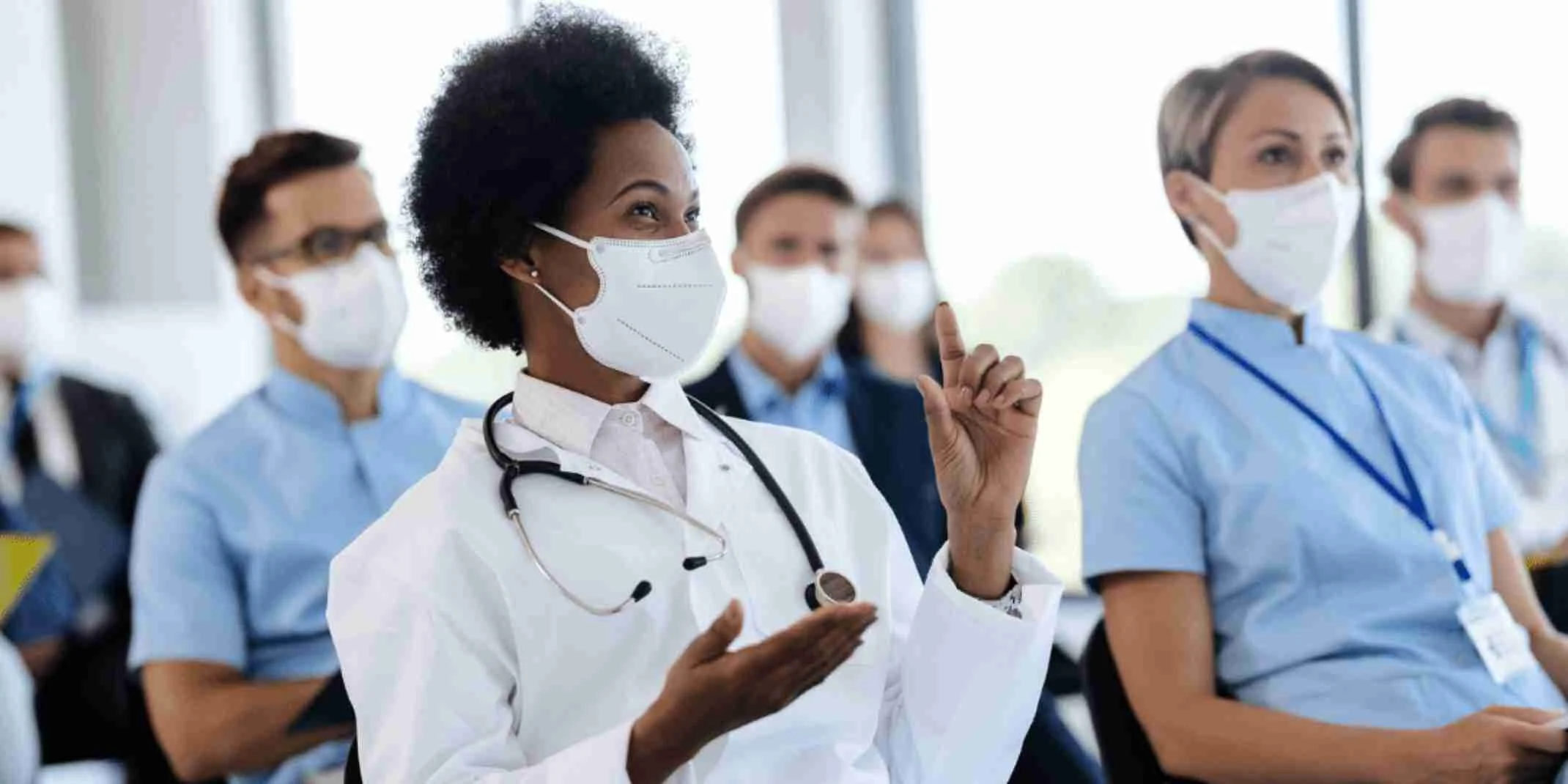 A Black woman physician animatedly asks a question in a class of clinicians.