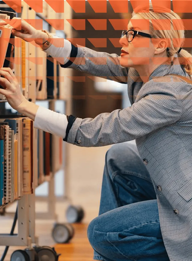 Serious business woman squatting in the bookshop and picking a book from a shelf