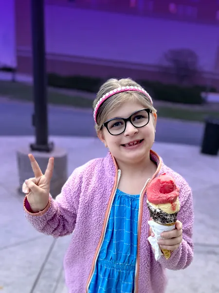 Young girl with rare disease flashing peace sign and holding an ice cream cone