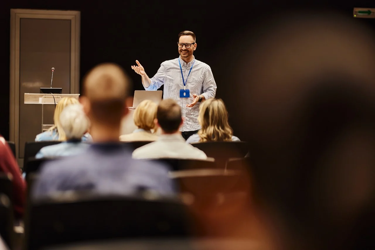 A man standing up facing committee members and speaking or leading a discussion