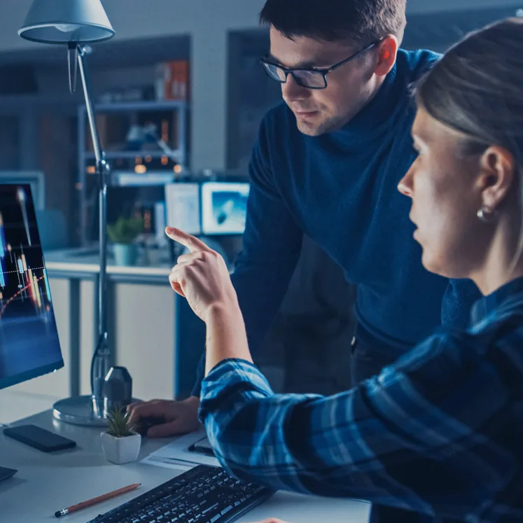 Two colleagues looking at computer in a dark room