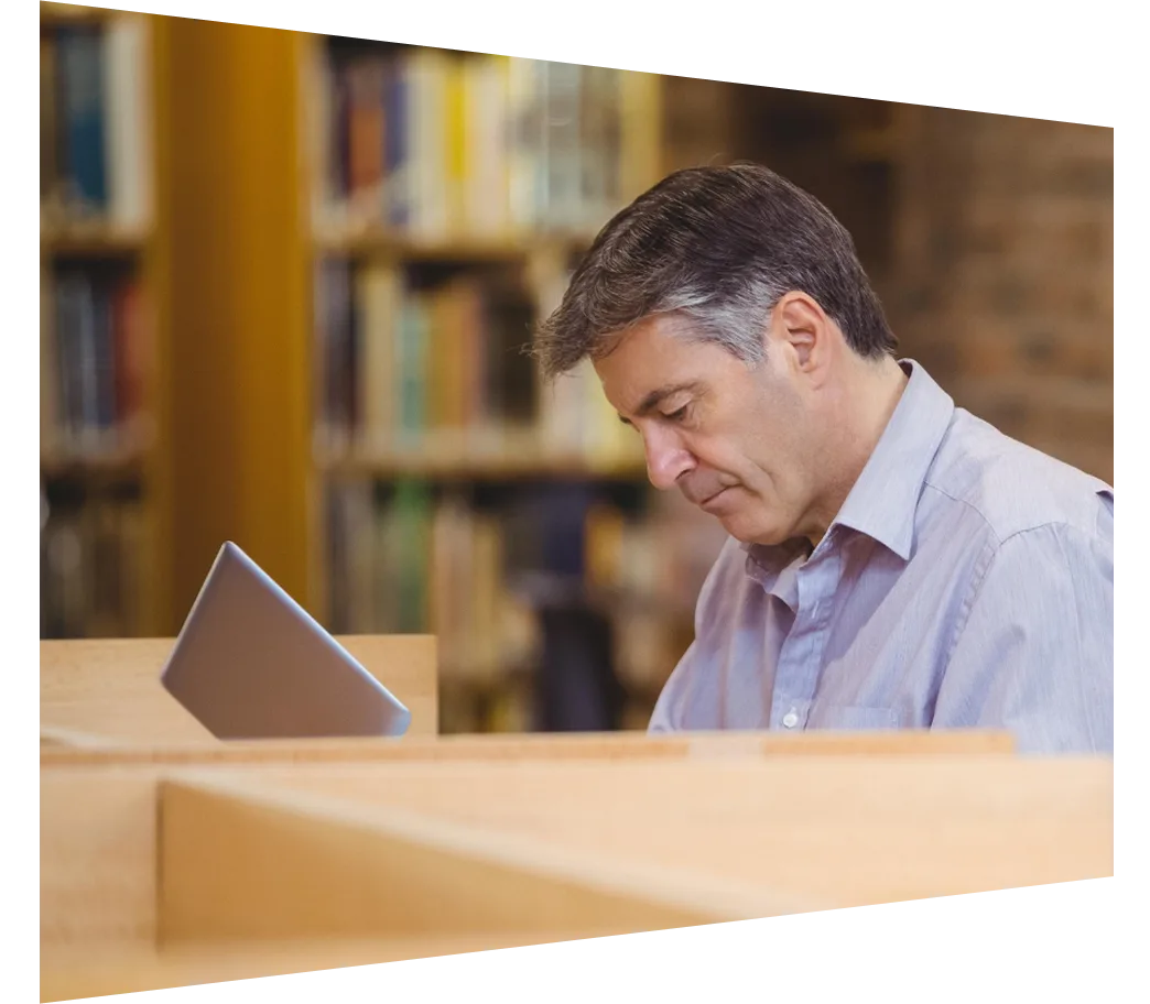 Man working at a library carrel with shelves of books and periodicals in the background