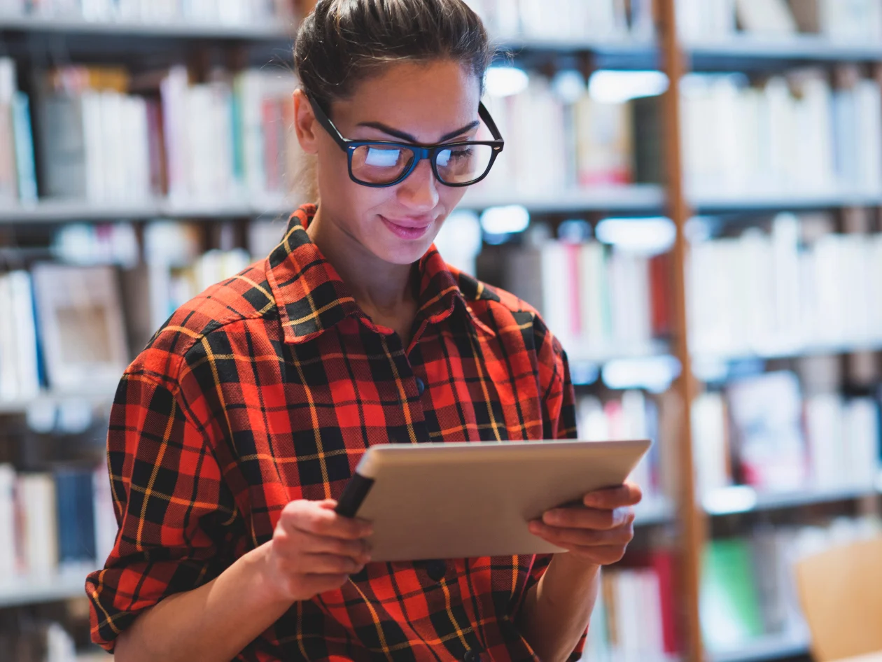 A woman in glasses looking down at an tablet