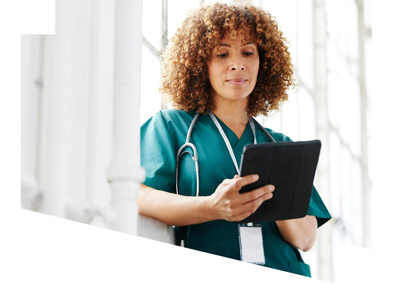 Female healthcare professional leaning against a window looking at a digital tablet