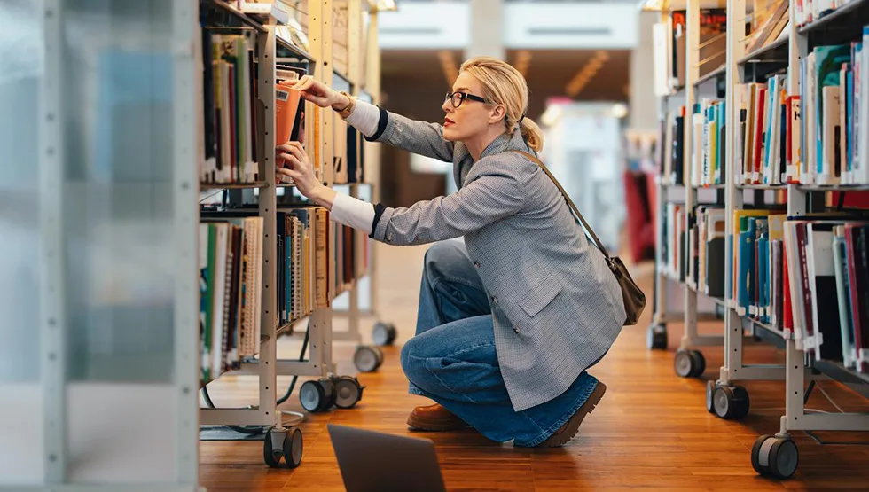 Businesswoman choosing a new book in the library - banner halfwidth