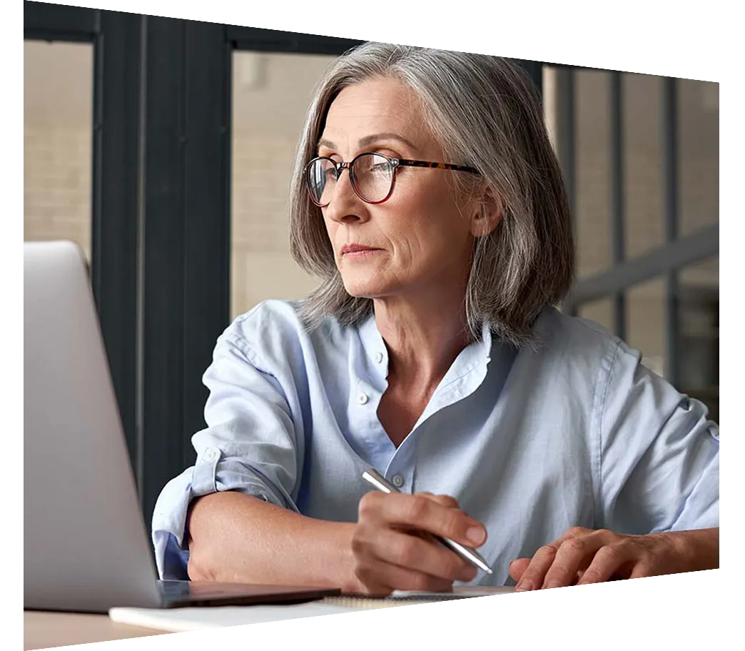 Mature woman sitting in front of laptop taking notes