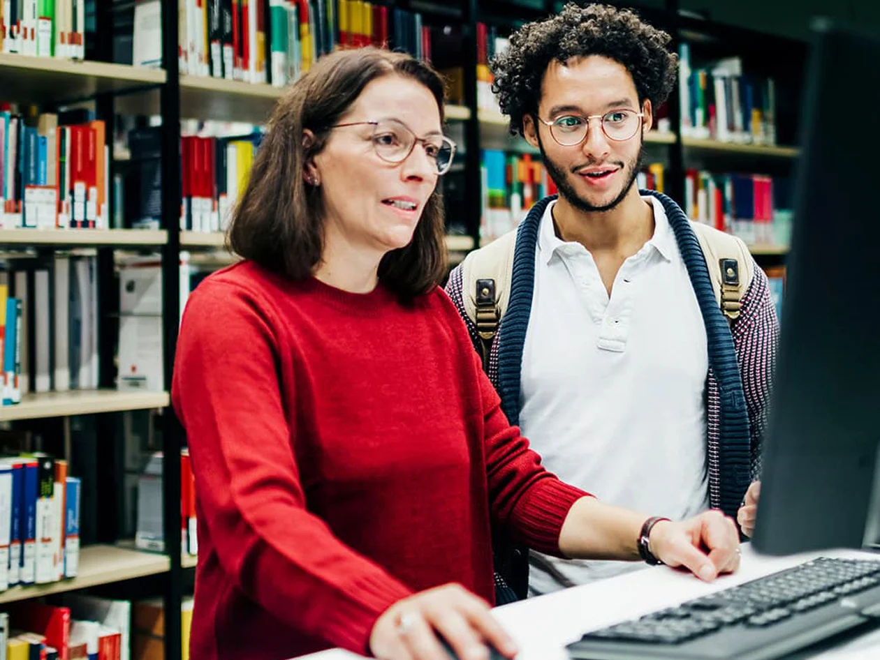 Librarian looking up books on computer for student