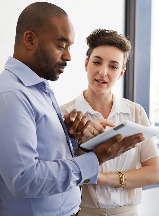 Coworkers standing next to wall looking at a tablet together