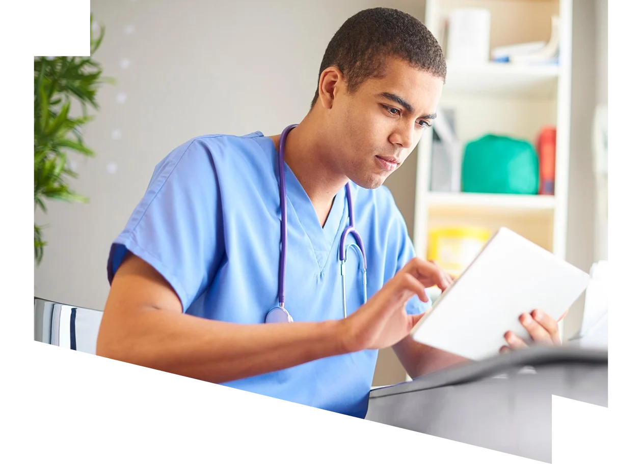 Male doctor wearing scrubs at his desk looking at digital tablet