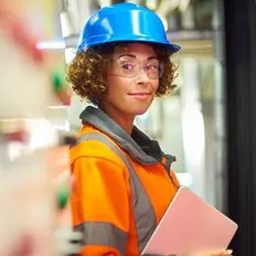 Female worker in industrial setting with hard hat and safety goggles