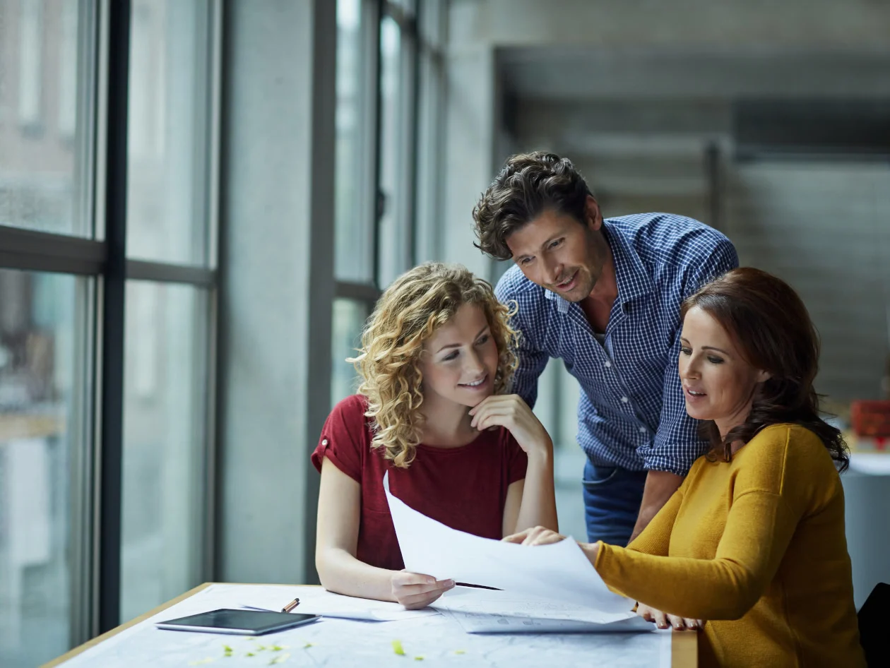 Three people standing around a table looking at a paper.