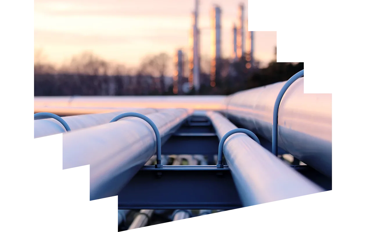 A series of pipes in the foreground with an oil refinery in the background