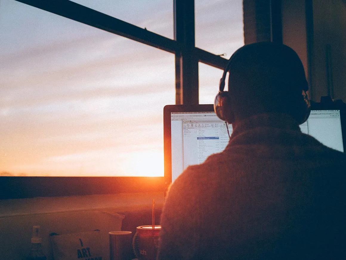 Man sitting facing a monitor with sunset in the background