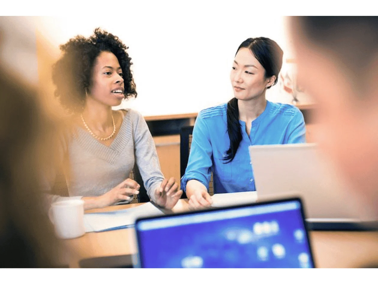 Woman having a conversation with another woman while sitting on a desk