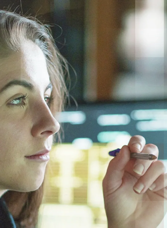 A woman working at a computer with a pen in her hand.