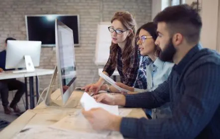 Three students looking at a desktop computer screen