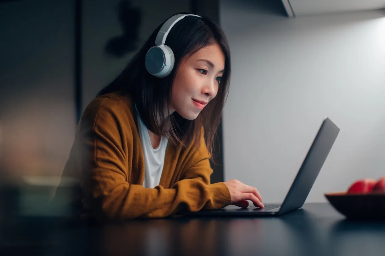 Young Asian woman with headphones while working on laptop at home