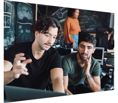 Two students in discussion with chalkboard in background