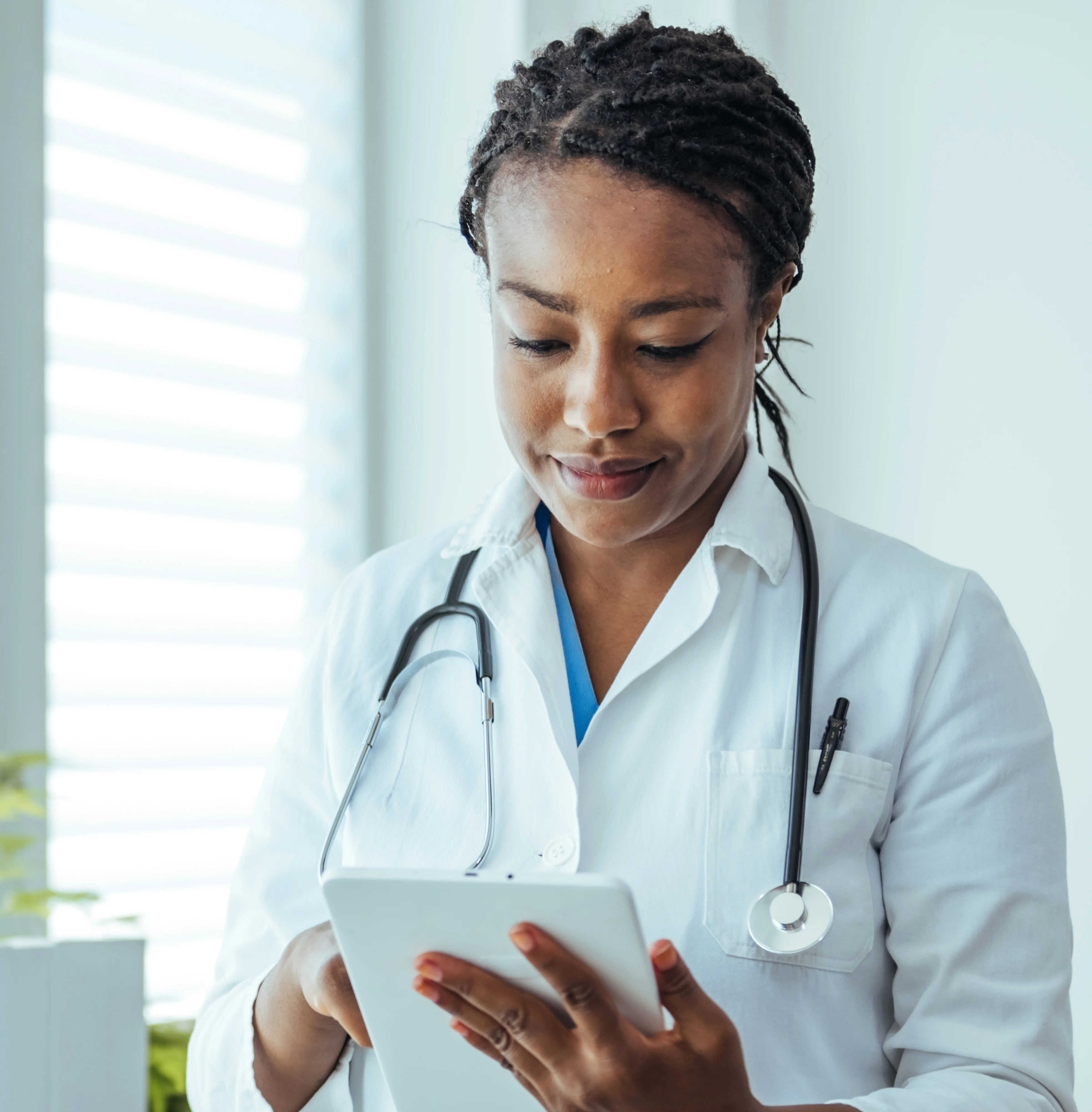 Female physician in a white coat with stethoscope looks at tablet.