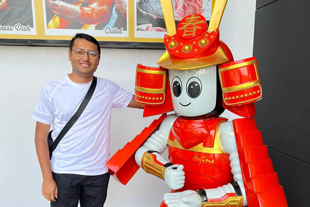HM Kamrul Hassan在泰国曼谷的Hajime机器人餐厅与人形机器人合影，机器人在餐厅接受订单并提供食物。他参观了这家餐厅，这是他与类人服务机器人合作的一部分。