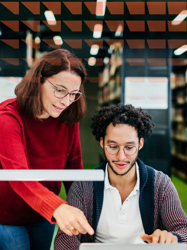 Librarian helping a young man working on his laptop in a public library