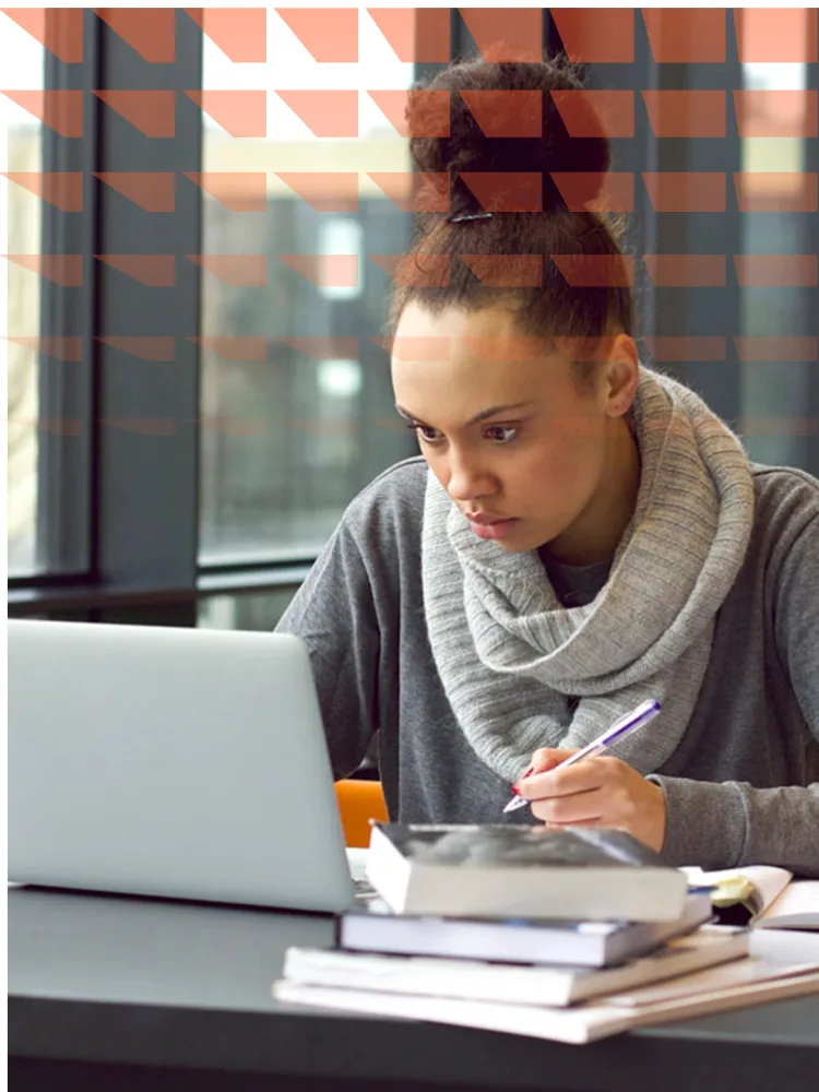 Young female student studying on a laptop and taking notes