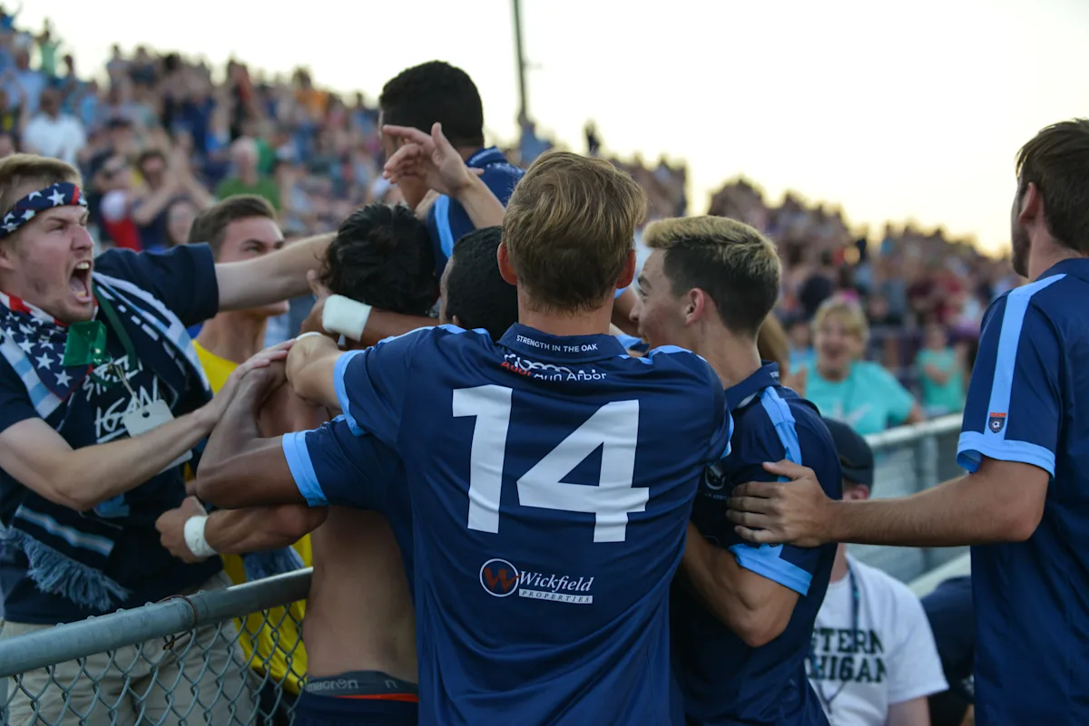 Main Street Hooligans and AFC Ann Arbor players celebrate a late winner at the fence