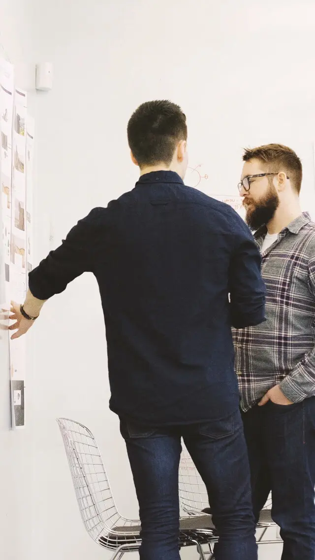 Two people discussing diagrams stuck to a whiteboard.