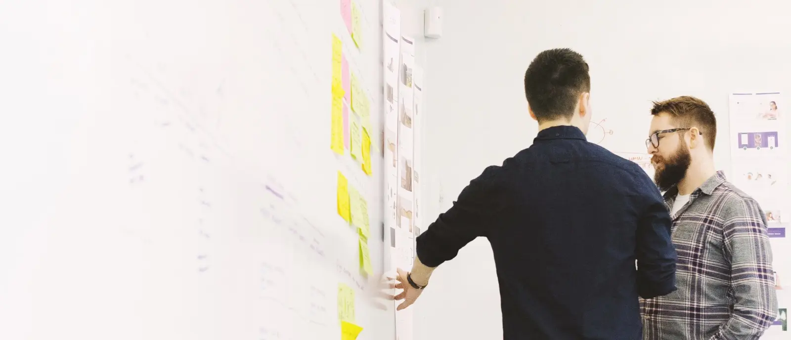 Two people discussing diagrams stuck to a whiteboard.