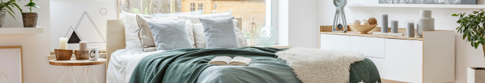 Ein helles Schlafzimmer, mit einem Bett, Nachttisch und einer Kommode