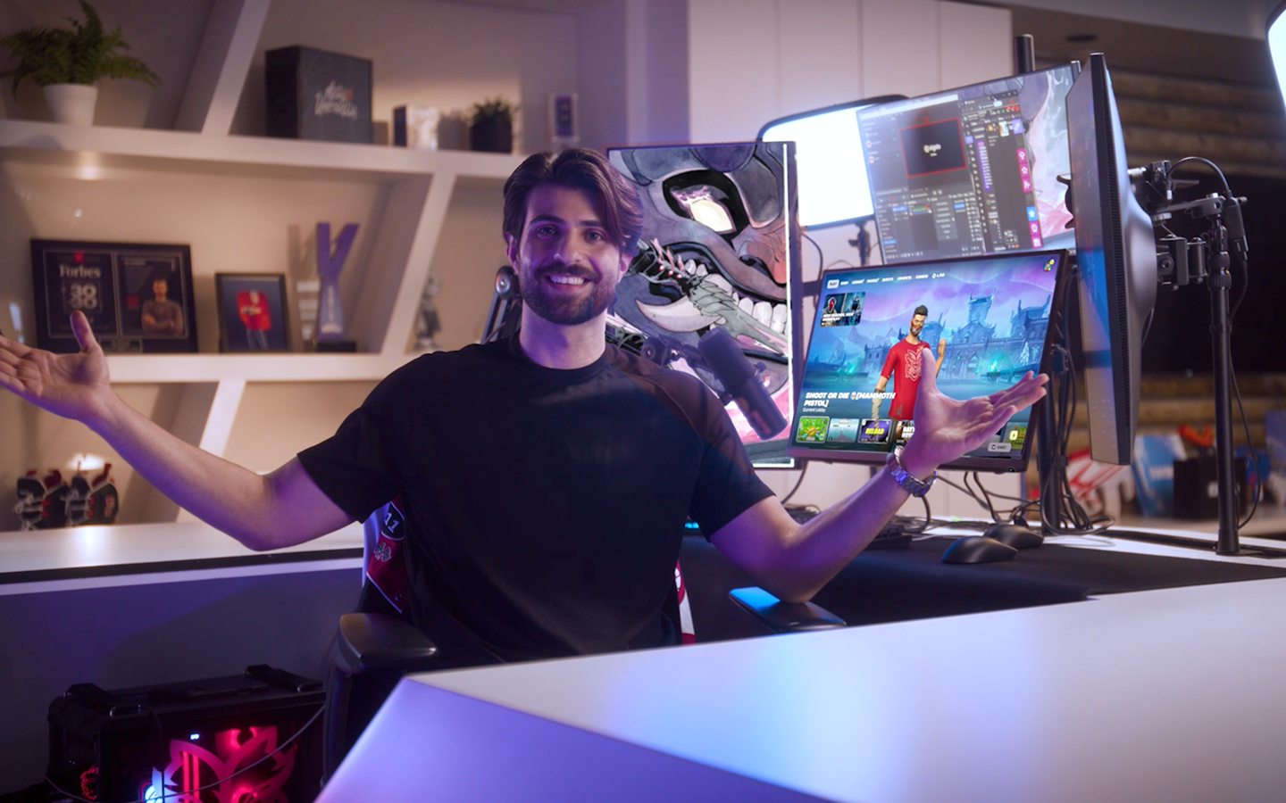 A man smiling, sitting in front of his computer set up with this arms up