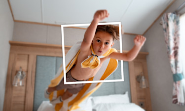 Toddler wearing a cape and diving onto his bed