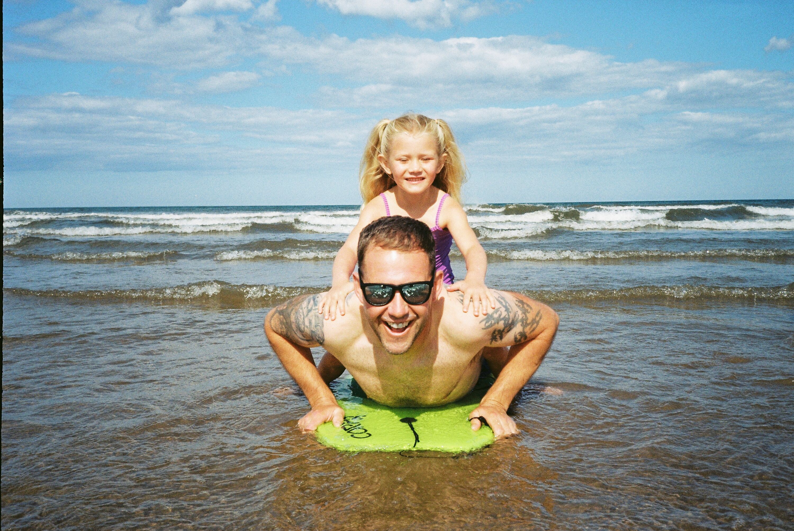 A dad uses a body board in the sea with his young daughter.
