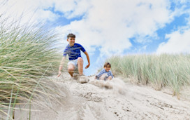 Two kids preparing to slide down a sand dune