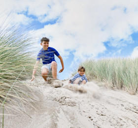 Two kids preparing to slide down a sand dune