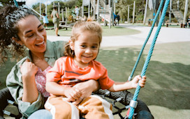 A mum and her son play on the swings at the park at Hafan y Mor.