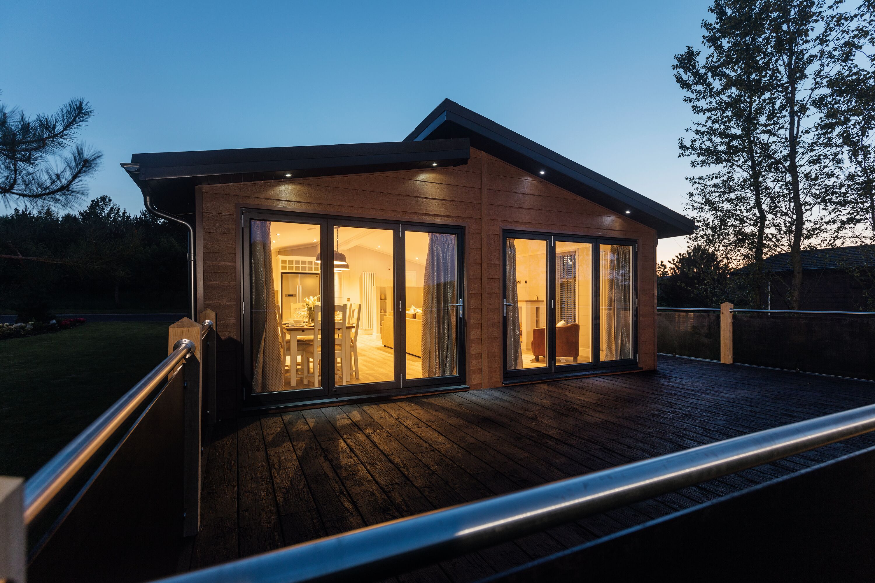A lodge viewed from the outside in the evening, with interior lights highlighting the cosy living space.