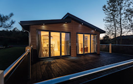 A lodge viewed from the outside in the evening, with interior lights highlighting the cosy living space.