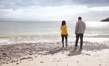 A couple stroll along the beach at Hafan Y Môr.