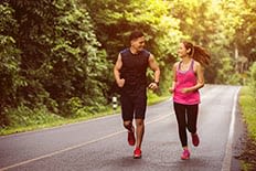 Un couple qui fait de la course à pieds à côté de la route, il y a des arbres des deux côtés de la route