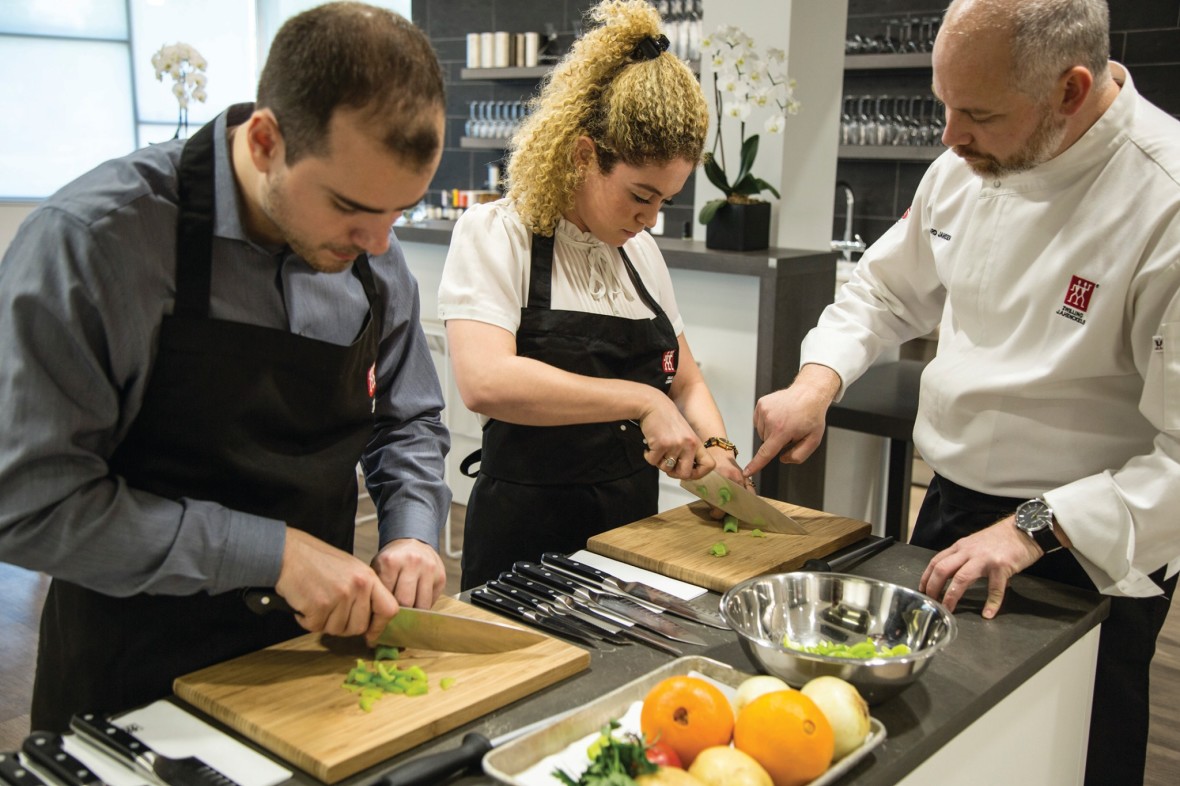 A Zwilling Cooking Studio chef instructing two students on knife skills