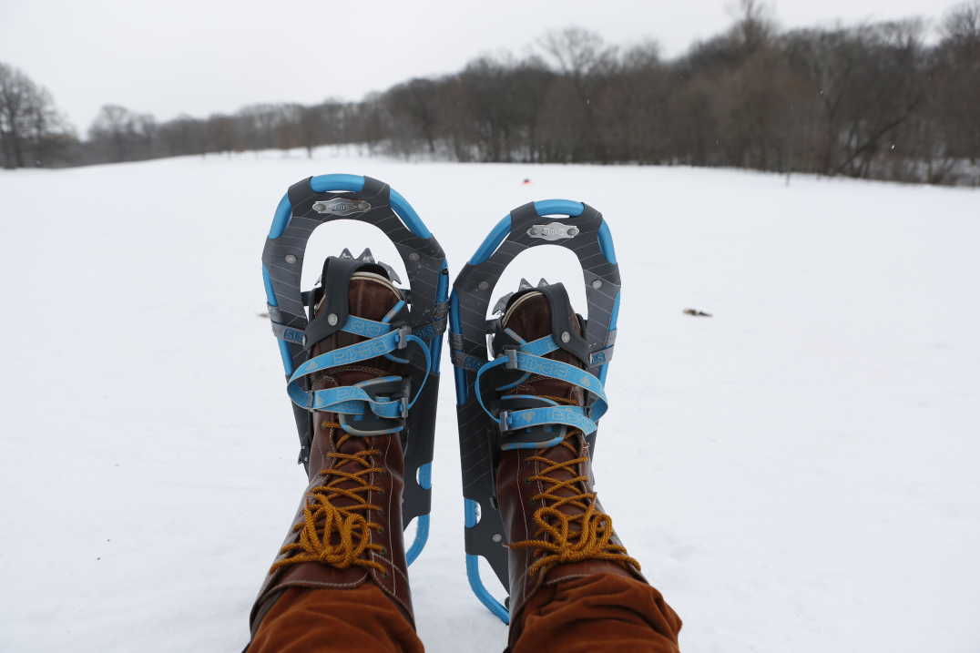 Two feet in boots and snowshoes in foreground and snow covered field in background