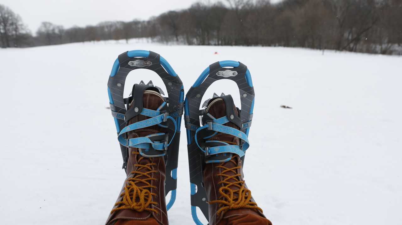 Two feet in boots and snowshoes in foreground and snow covered field in background