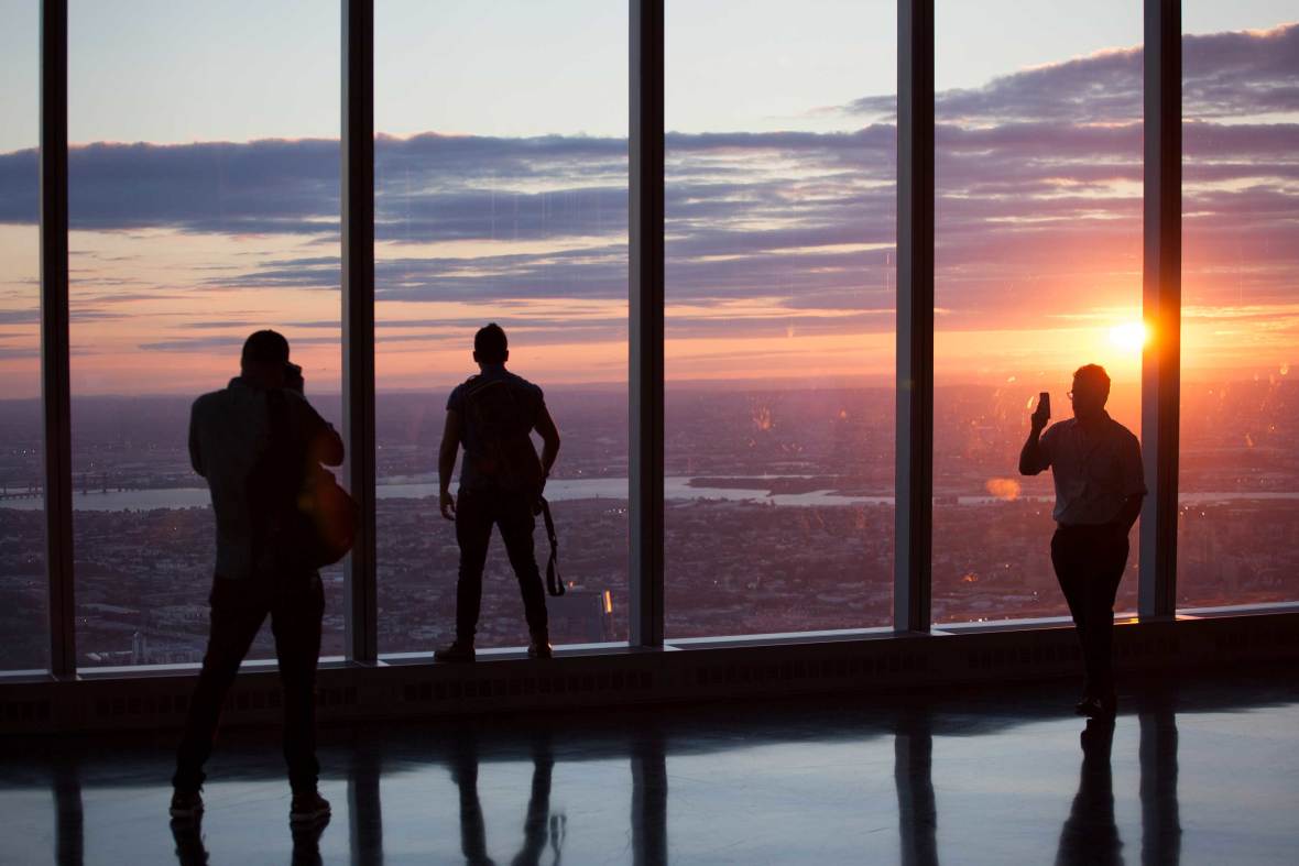 Three people silhouetted against an orange, pink and purple sunset at the One World Observatory